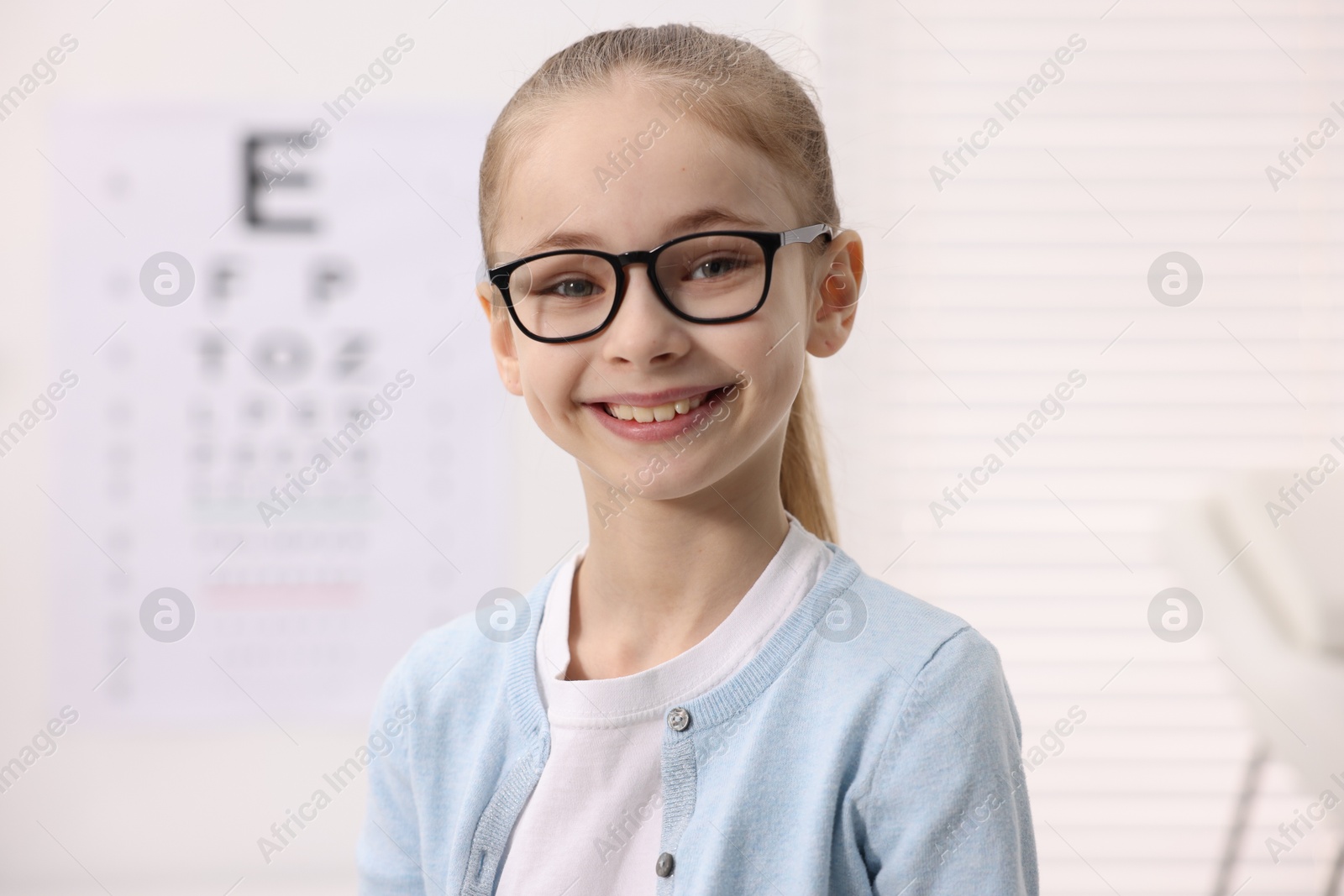 Photo of Little girl wearing glasses near vision test chart at ophthalmologist office