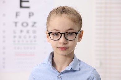 Photo of Little girl wearing glasses near vision test chart at ophthalmologist office