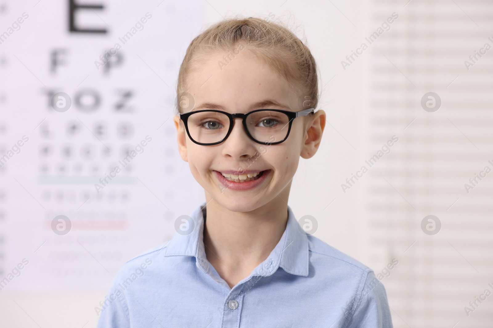 Photo of Little girl wearing glasses near vision test chart at ophthalmologist office