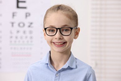 Photo of Little girl wearing glasses near vision test chart at ophthalmologist office