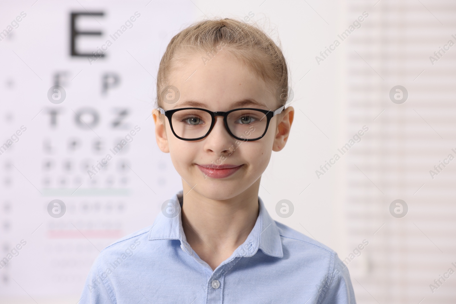 Photo of Little girl wearing glasses near vision test chart at ophthalmologist office