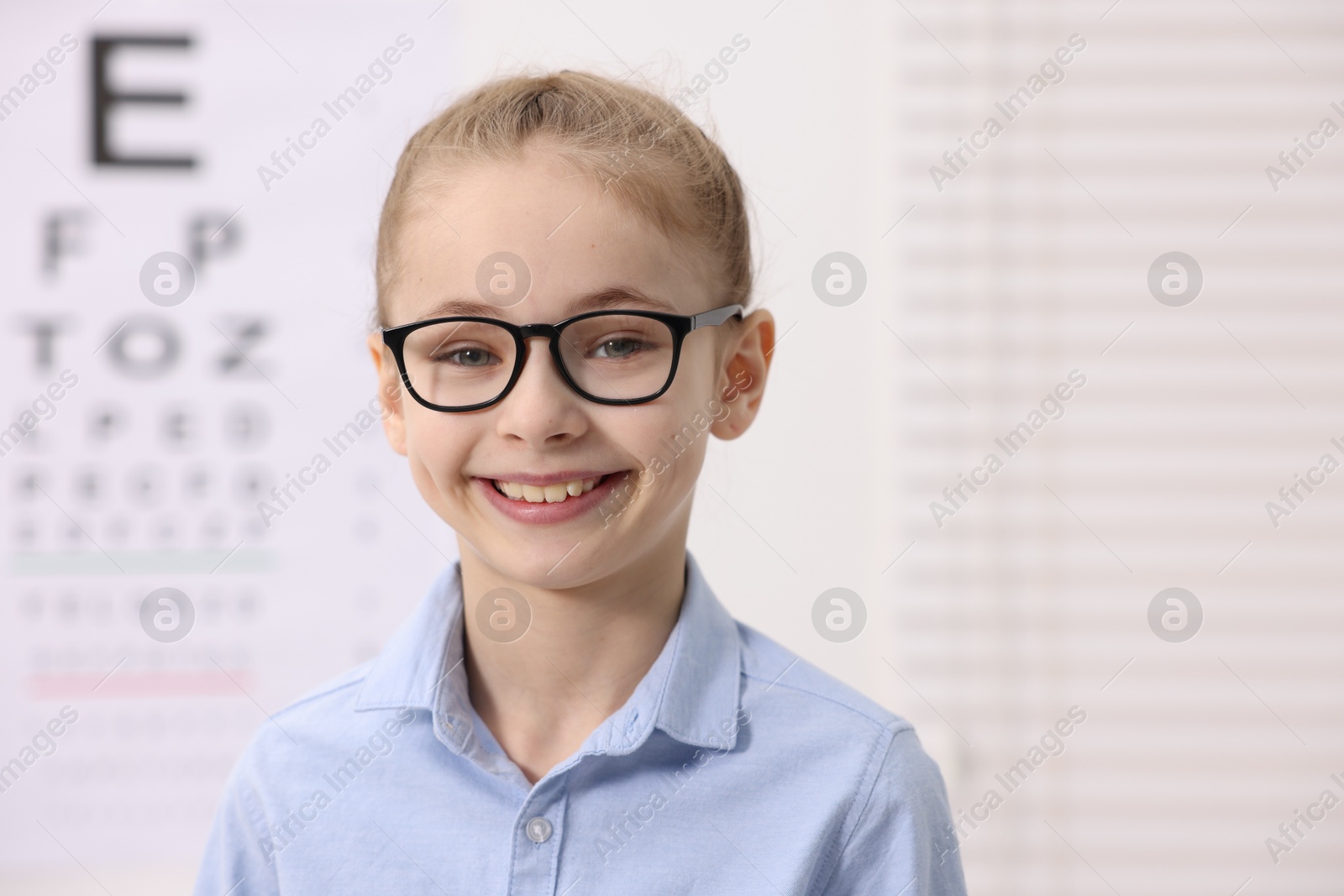 Photo of Little girl wearing glasses near vision test chart at ophthalmologist office