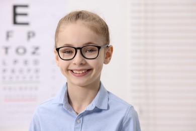 Photo of Little girl wearing glasses near vision test chart at ophthalmologist office