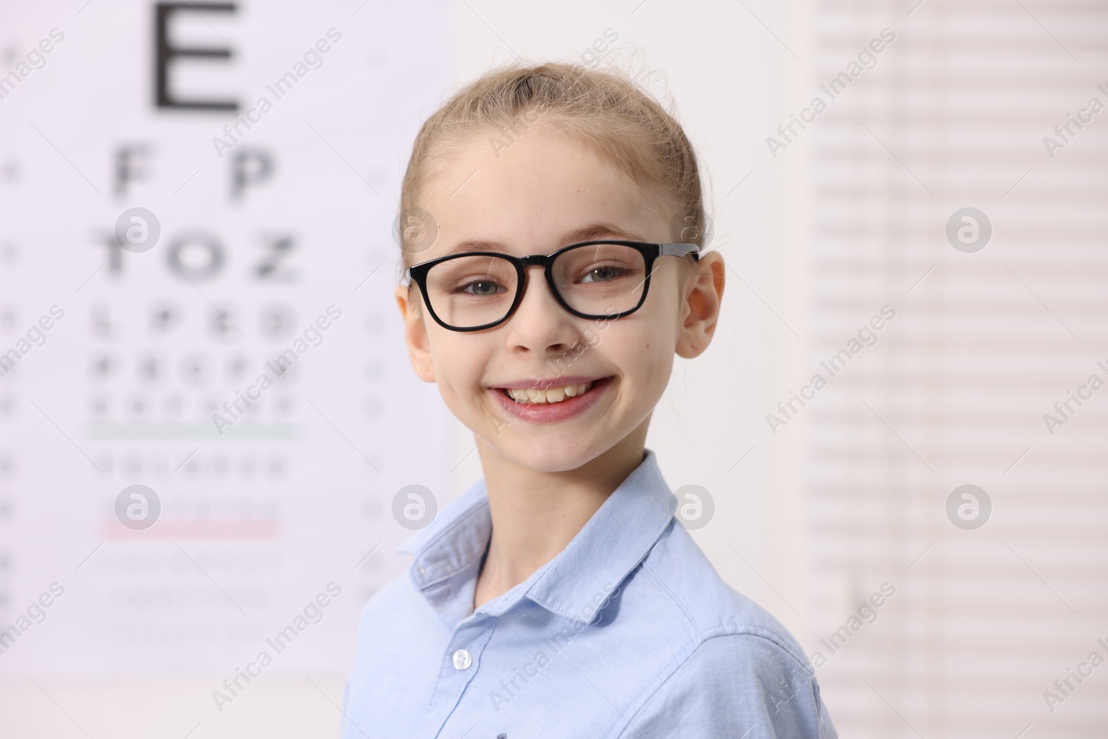 Photo of Little girl wearing glasses near vision test chart at ophthalmologist office