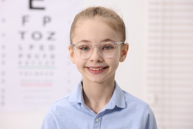 Photo of Little girl wearing glasses near vision test chart at ophthalmologist office