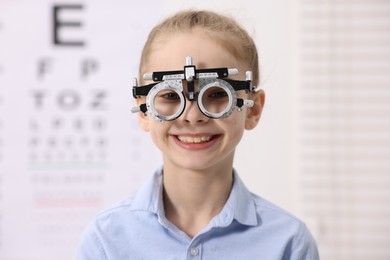 Photo of Little girl with trial frame near vision test chart at ophthalmologist office