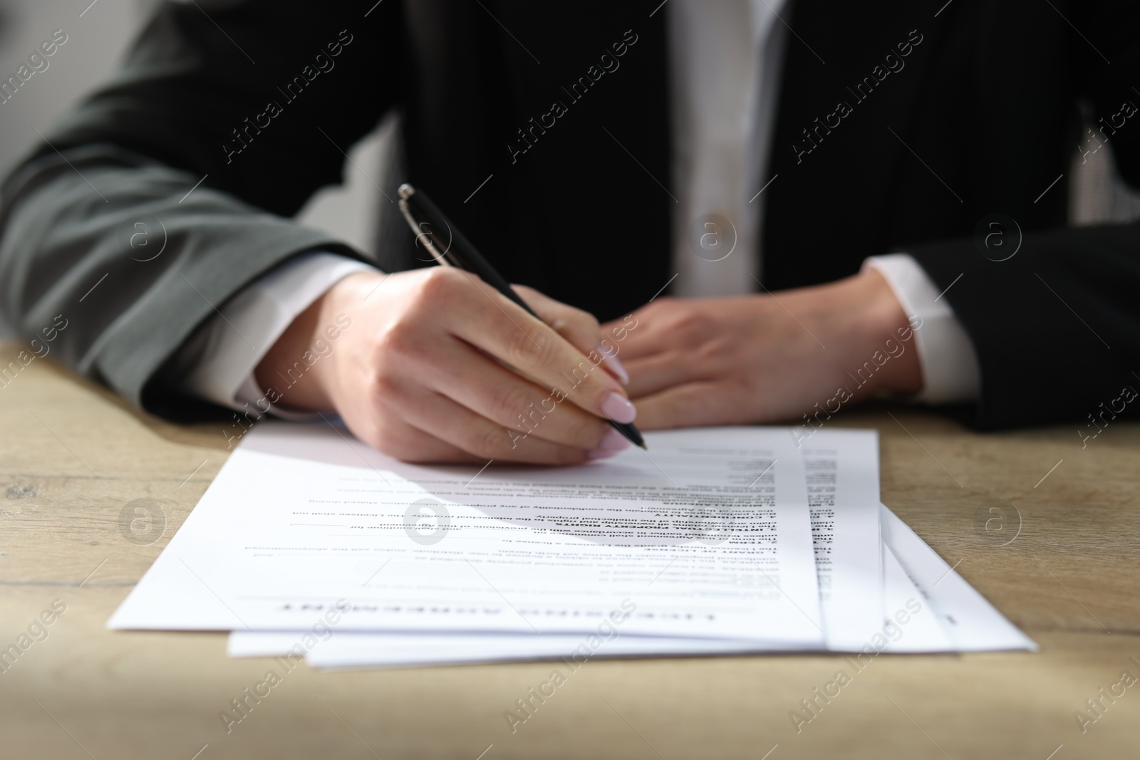 Photo of Woman signing licensing agreement document at wooden table indoors, closeup