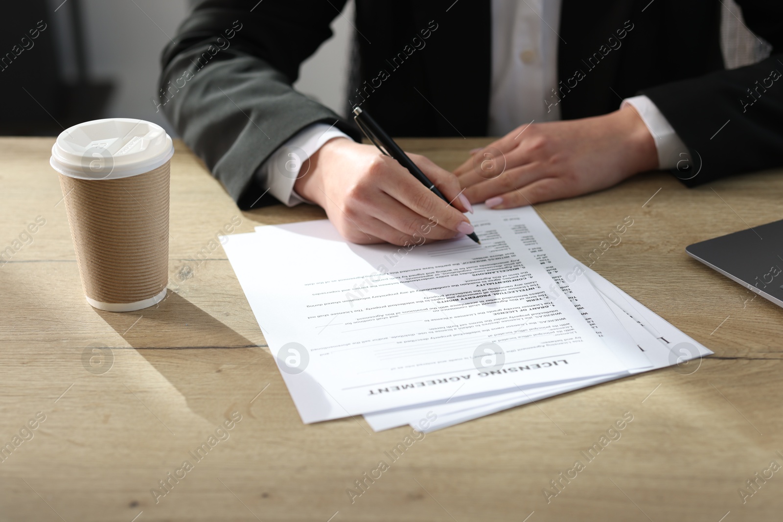 Photo of Woman signing licensing agreement document at wooden table indoors, closeup