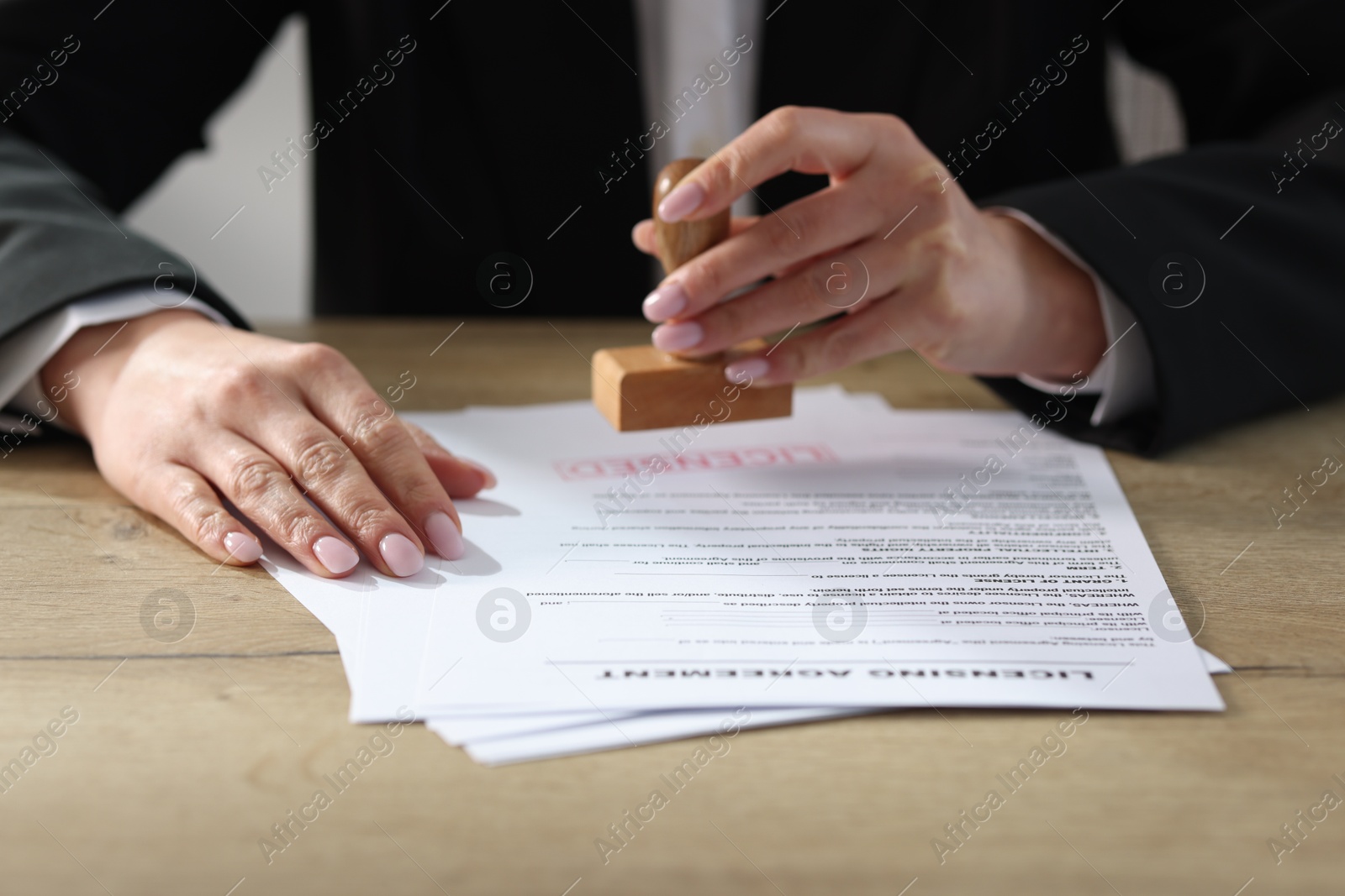 Photo of Woman stamping licensing agreement document at wooden table indoors, closeup