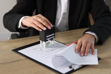 Photo of Woman stamping licensing agreement document at wooden table indoors, closeup