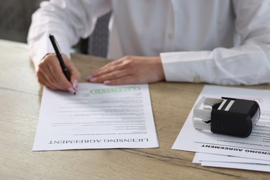 Photo of Woman signing licensing agreement document at wooden table indoors, closeup