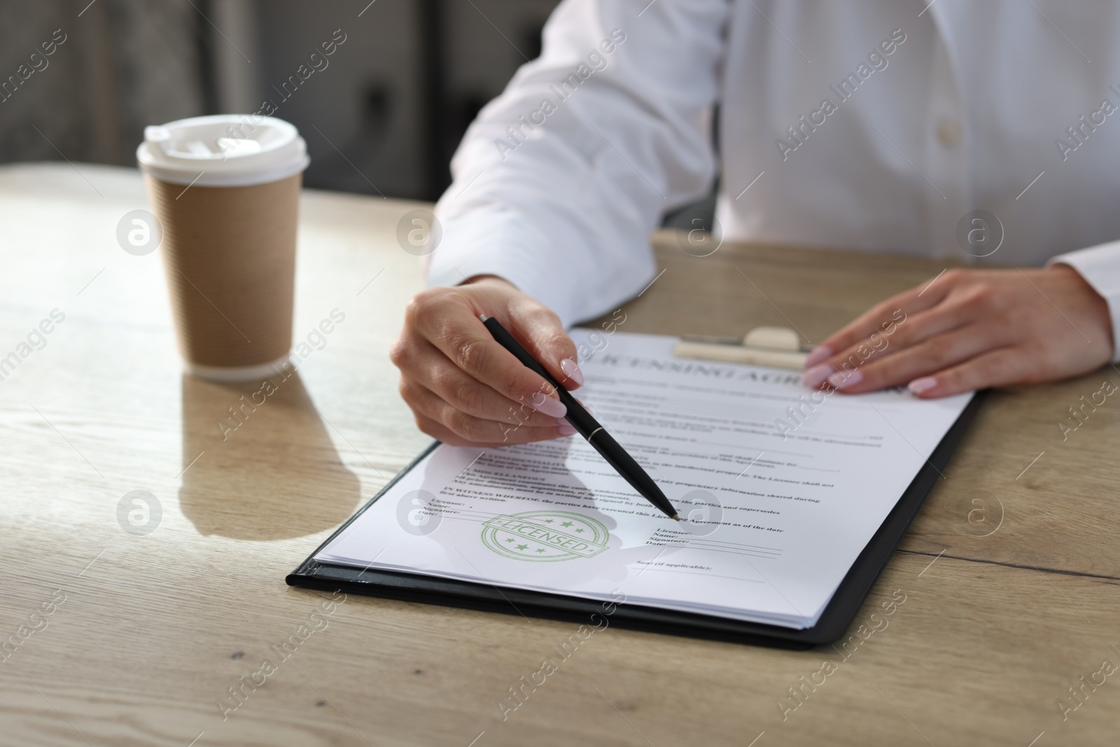 Photo of Woman with pen pointing at licensing agreement document at wooden table indoors, closeup