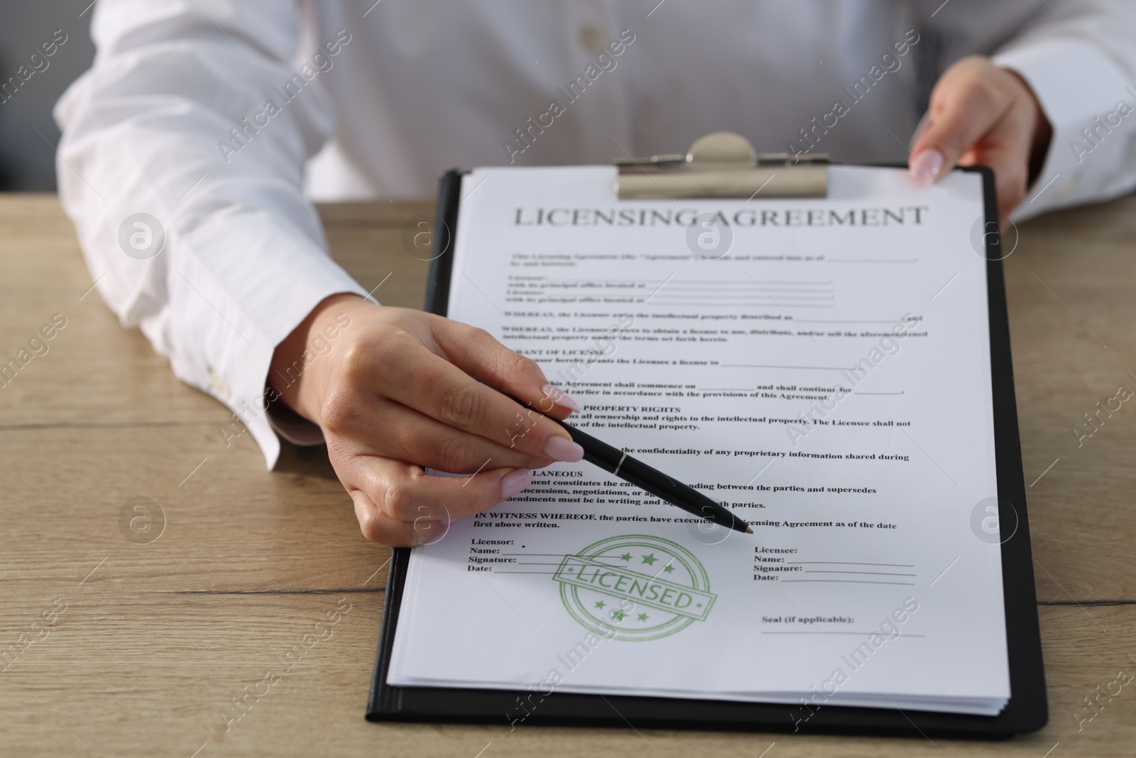 Photo of Woman with pen pointing at licensing agreement document at wooden table indoors, closeup