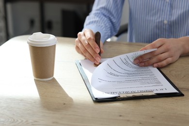 Photo of Woman stamping licensing agreement document at wooden table indoors, closeup