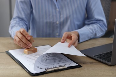 Photo of Woman stamping licensing agreement document at wooden table indoors, closeup