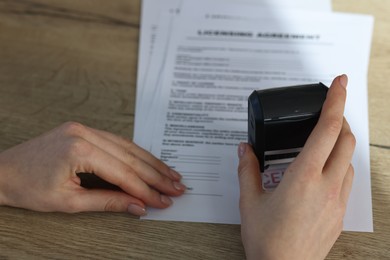 Photo of Woman stamping licensing agreement document at wooden table, closeup