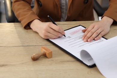 Photo of Woman signing licensing agreement document at wooden table indoors, closeup