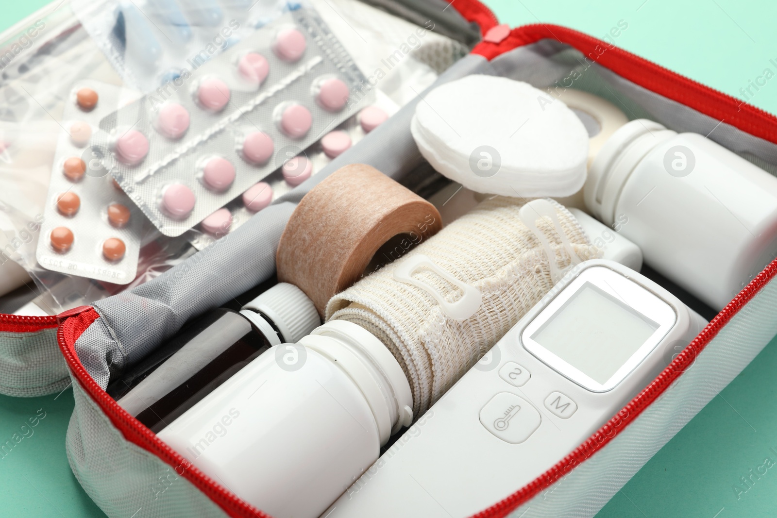 Photo of First aid kit. Different medical supplies in bag on turquoise background, closeup
