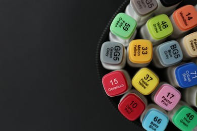 Many colorful marker pens in holder on black background, top view. Space for text