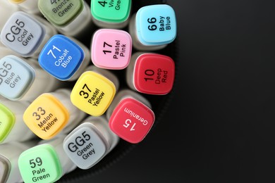 Many colorful marker pens in holder on black background, top view. Space for text