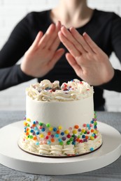 Photo of Woman refusing to eat cake at grey wooden table, selective focus. Food allergy concept