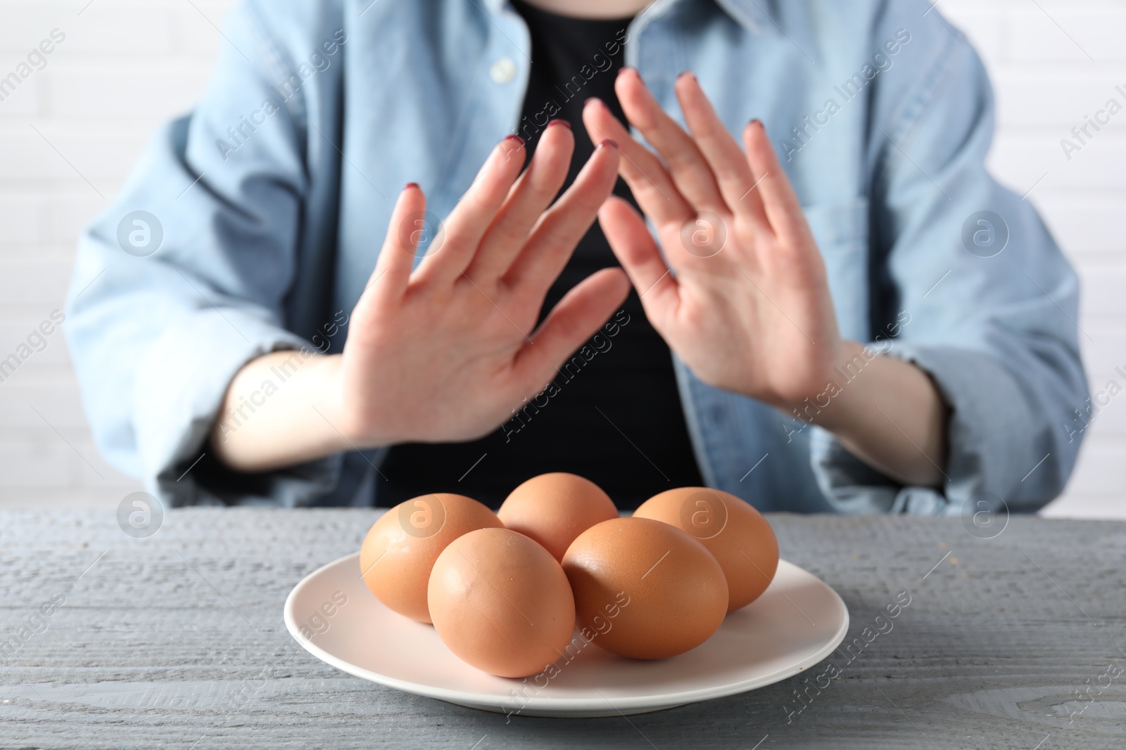 Photo of Woman refusing to eat eggs at grey wooden table, selective focus. Food allergy concept