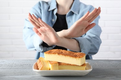 Photo of Woman refusing to eat cheesecake at grey wooden table, selective focus. Food allergy concept