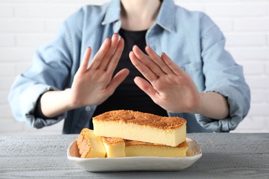 Photo of Woman refusing to eat cheesecake at grey wooden table, selective focus. Food allergy concept