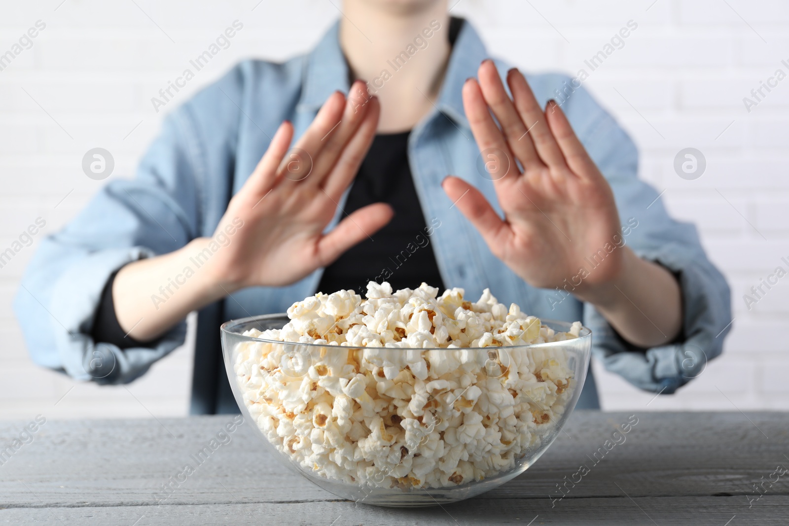 Photo of Woman refusing to eat popcorn at grey wooden table, selective focus. Food allergy concept