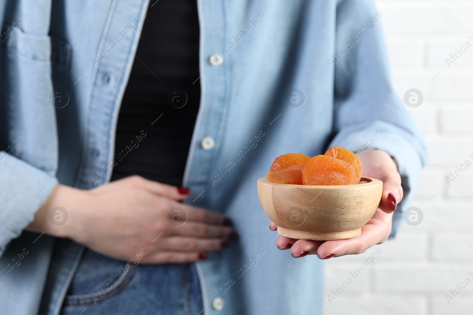 Photo of Woman refusing to eat dried apricots near white brick wall, closeup. Food allergy concept