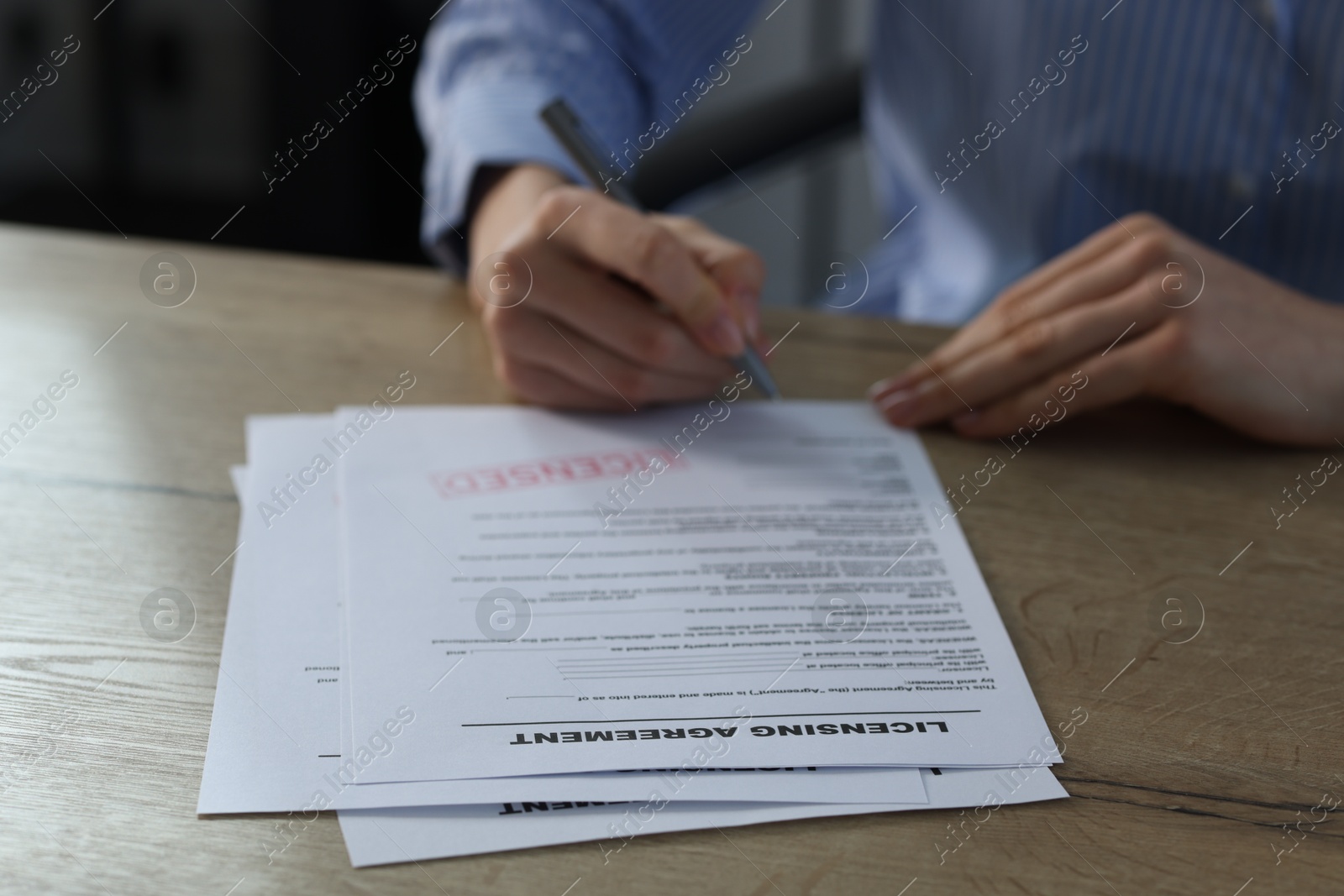 Photo of Woman signing licensing agreement document at wooden table indoors, closeup