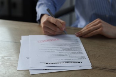 Photo of Woman signing licensing agreement document at wooden table indoors, closeup