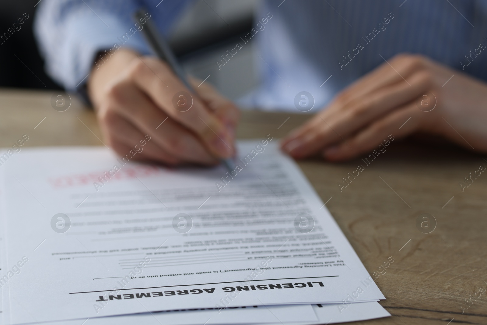 Photo of Woman signing licensing agreement document at wooden table indoors, closeup