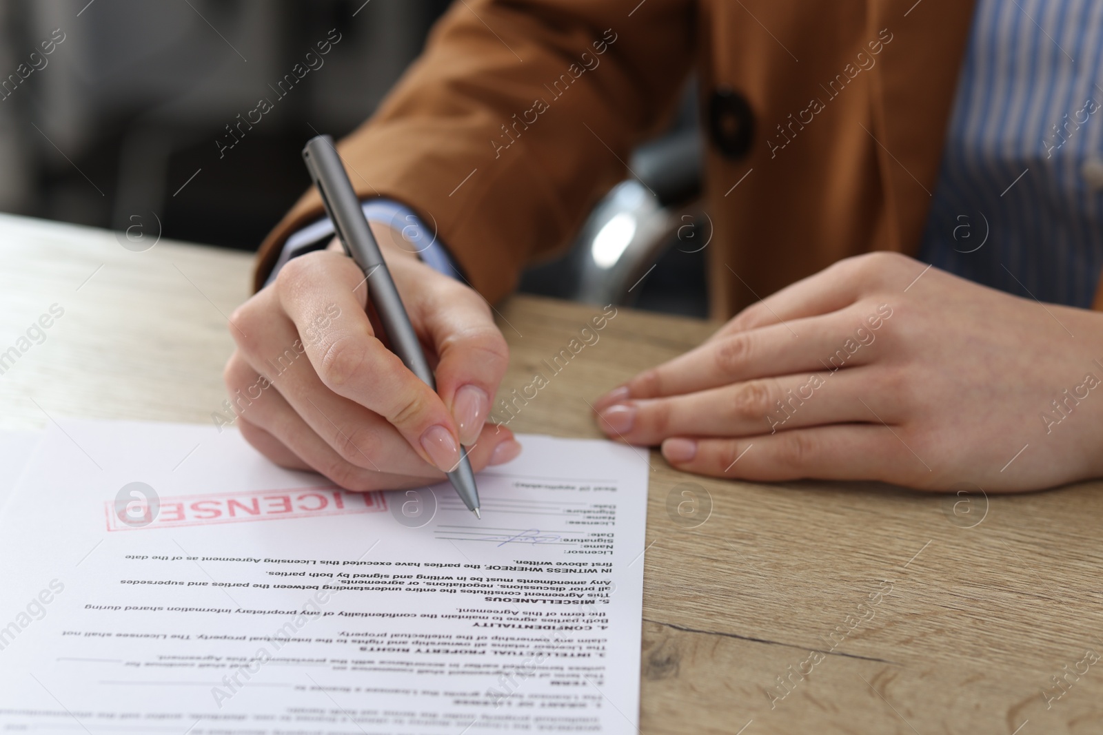 Photo of Woman signing licensing agreement document at wooden table indoors, closeup