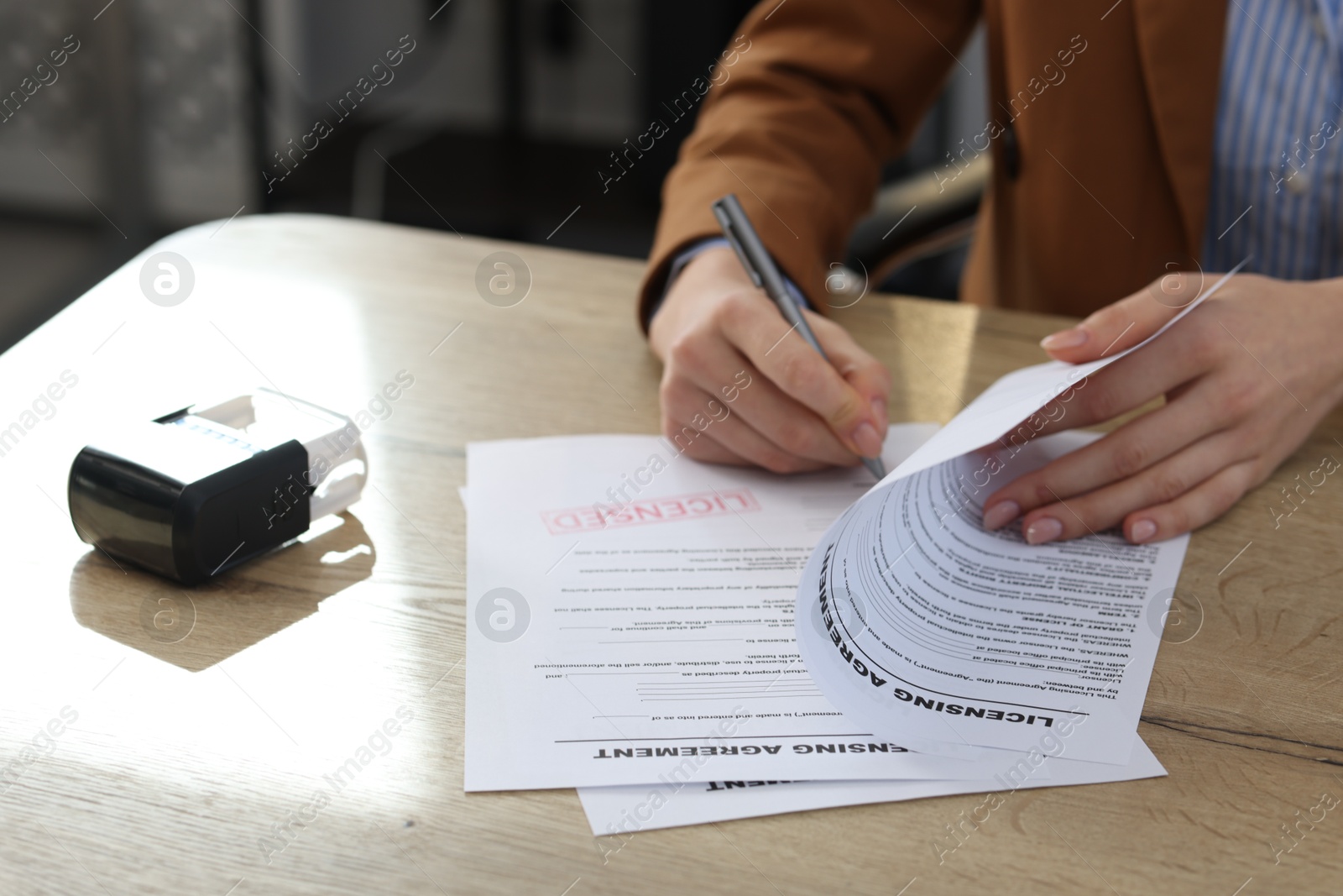 Photo of Woman signing licensing agreement document at wooden table indoors, closeup