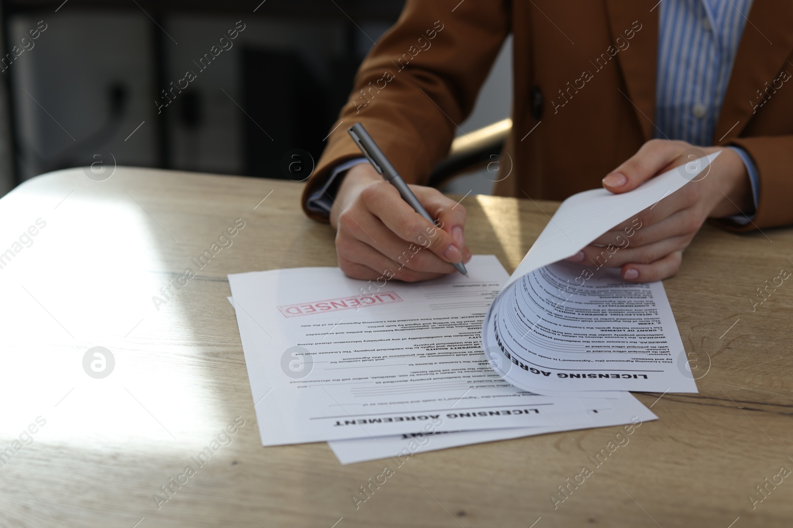 Photo of Woman signing licensing agreement document at wooden table indoors, closeup