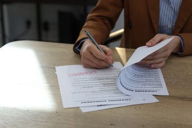 Photo of Woman signing licensing agreement document at wooden table indoors, closeup