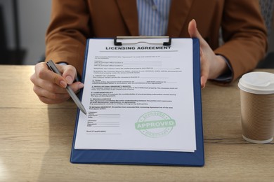 Photo of Woman with pen pointing at licensing agreement document at wooden table indoors, closeup