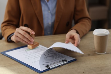 Photo of Woman stamping licensing agreement document at wooden table indoors, closeup