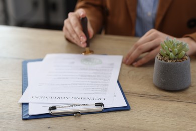 Photo of Woman stamping licensing agreement document at wooden table indoors, closeup