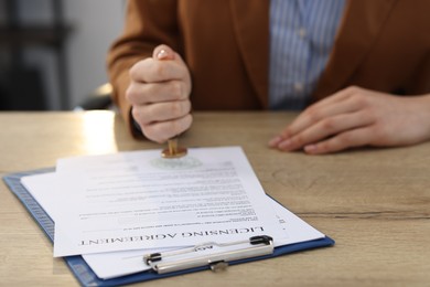 Photo of Woman stamping licensing agreement document at wooden table indoors, closeup