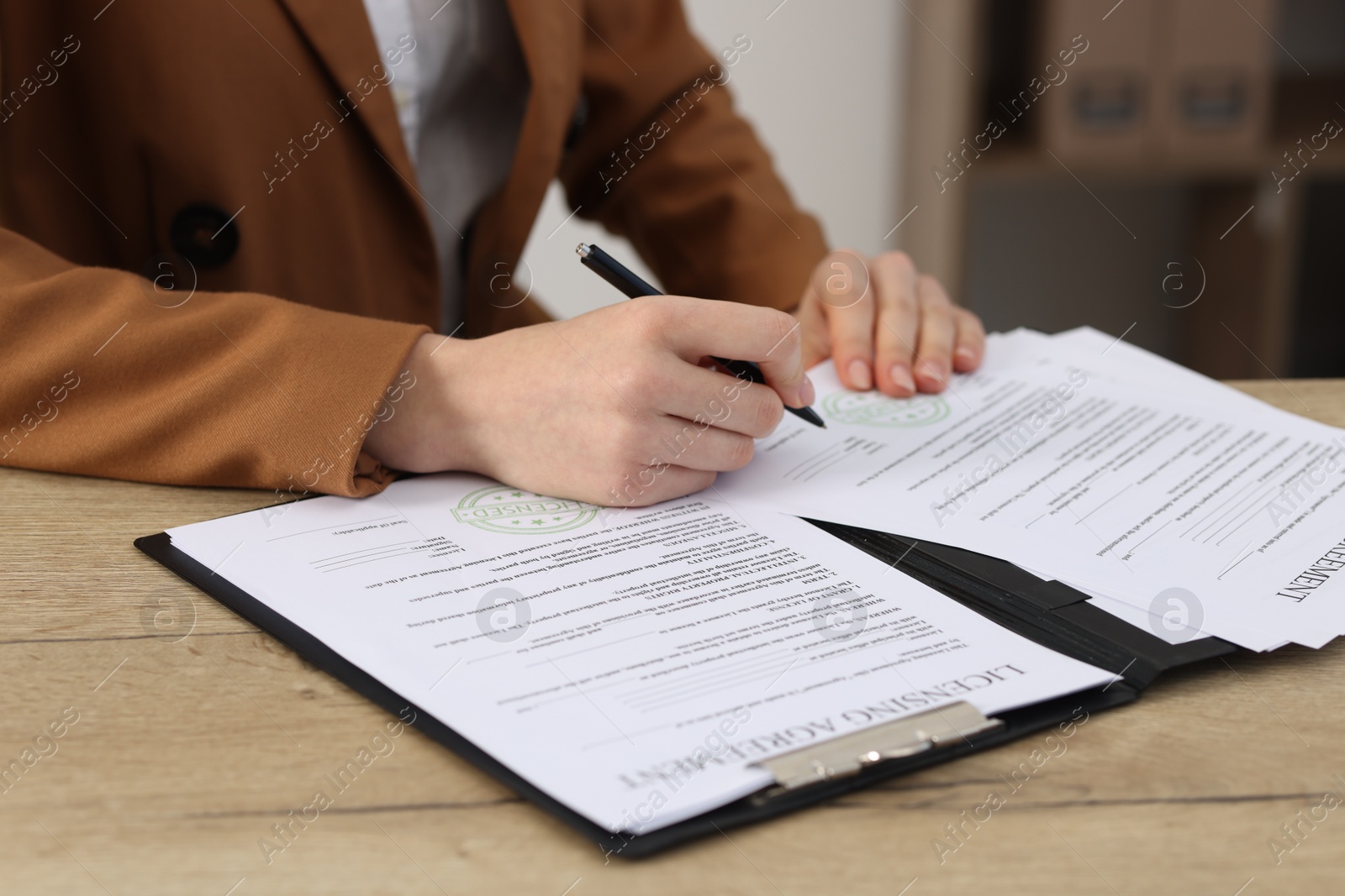 Photo of Woman signing licensing agreement document at wooden table indoors, closeup