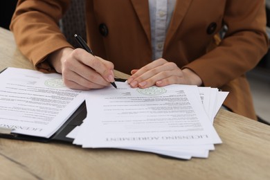 Photo of Woman signing licensing agreement document at wooden table indoors, closeup