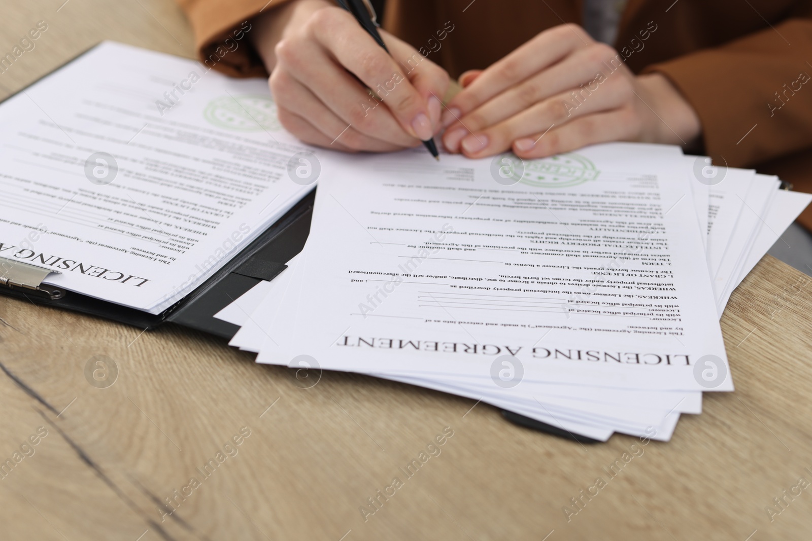 Photo of Woman signing licensing agreement document at wooden table indoors, closeup