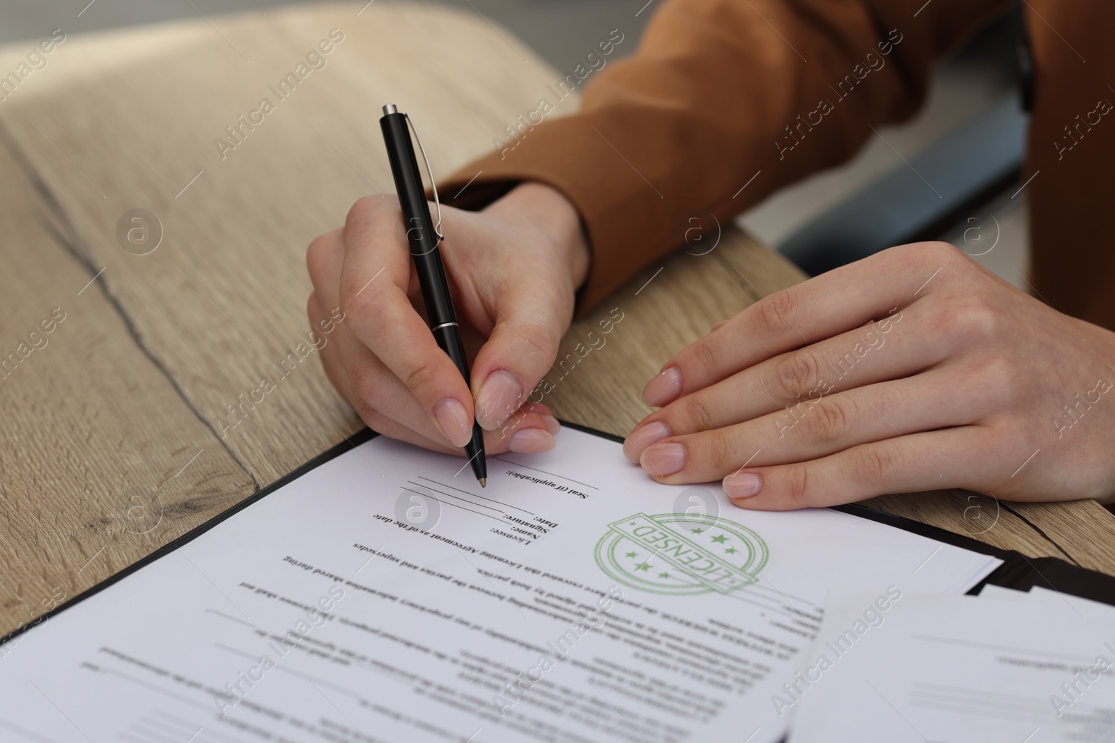 Photo of Woman signing licensing agreement document at wooden table indoors, closeup