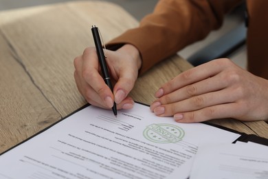 Photo of Woman signing licensing agreement document at wooden table indoors, closeup