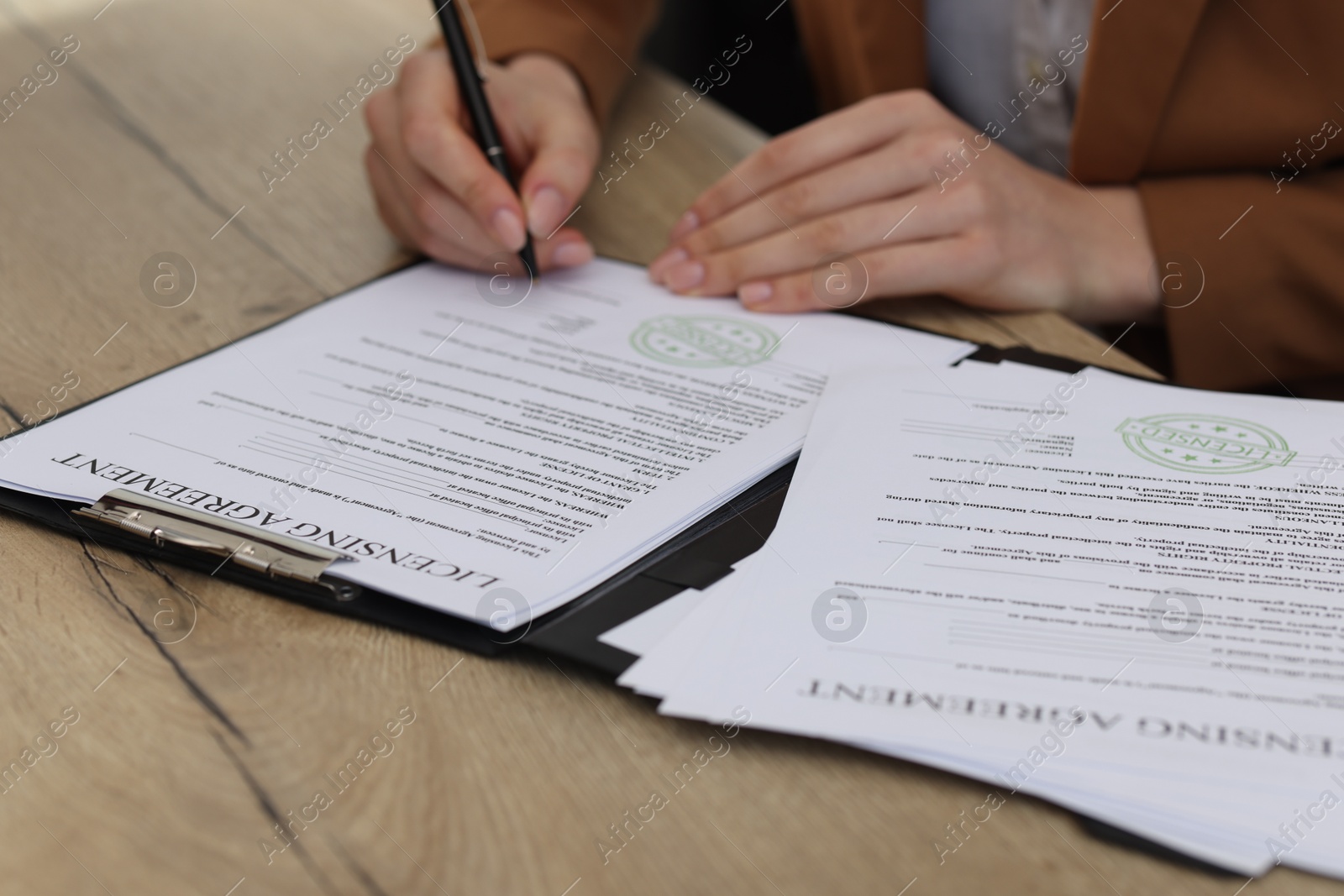 Photo of Woman signing licensing agreement document at wooden table indoors, closeup