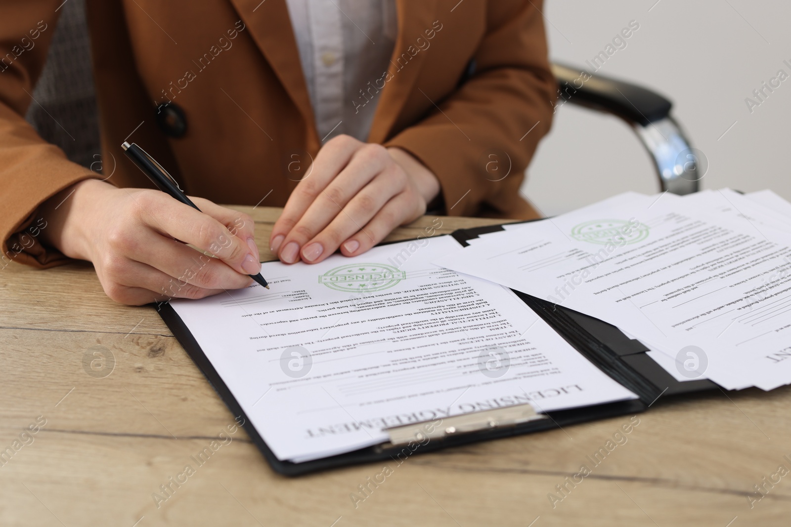 Photo of Woman signing licensing agreement document at wooden table indoors, closeup