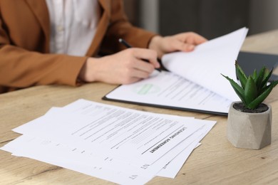 Photo of Woman signing licensing agreement document at wooden table indoors, selective focus