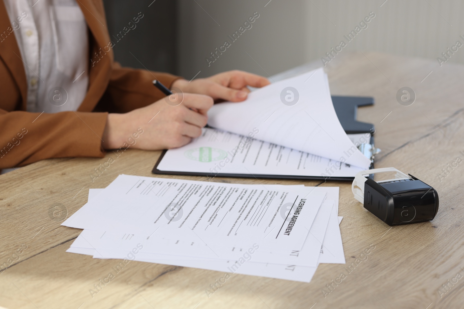 Photo of Woman signing licensing agreement document at wooden table indoors, closeup